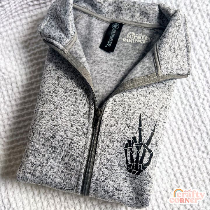 Folded view of heather grey Build Your Boneyard fleece zip-up jacket by Mel's Crafty Corner