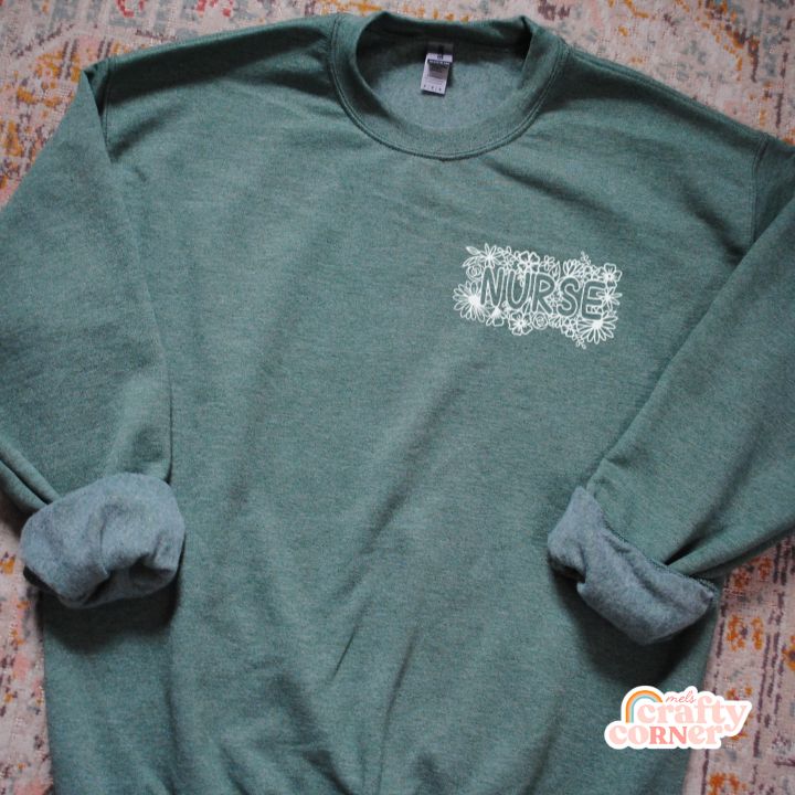 Flat lay view of green Pocket Floral Nurse classic crewneck sweatshirt by Mel's Crafty Corner