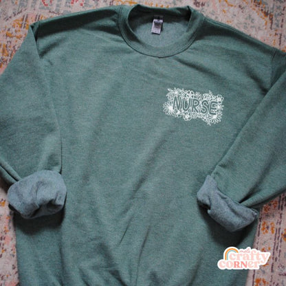 Flat lay view of green Pocket Floral Nurse classic crewneck sweatshirt by Mel's Crafty Corner