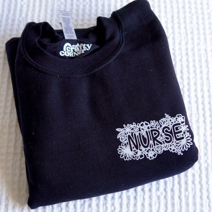 Folded view of black Pocket Floral Nurse classic crewneck sweatshirt by Mel's Crafty Corner