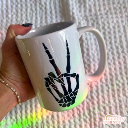 Peace sign hand gesture with Skeleton Boneyard 15 oz ceramic mug showing lifestyle usage by Mel's Crafty Corner